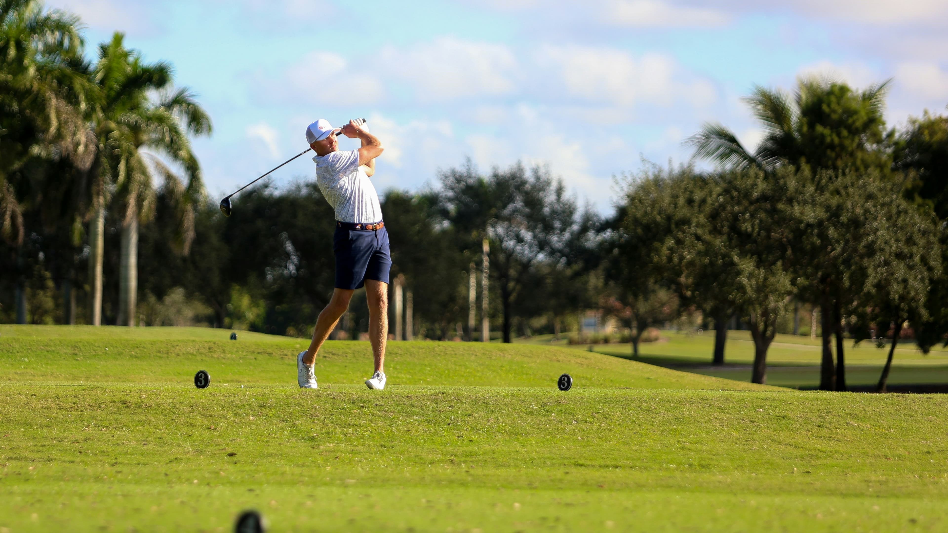 Golfer swinging a driver at a golf course in South Florida with palm trees